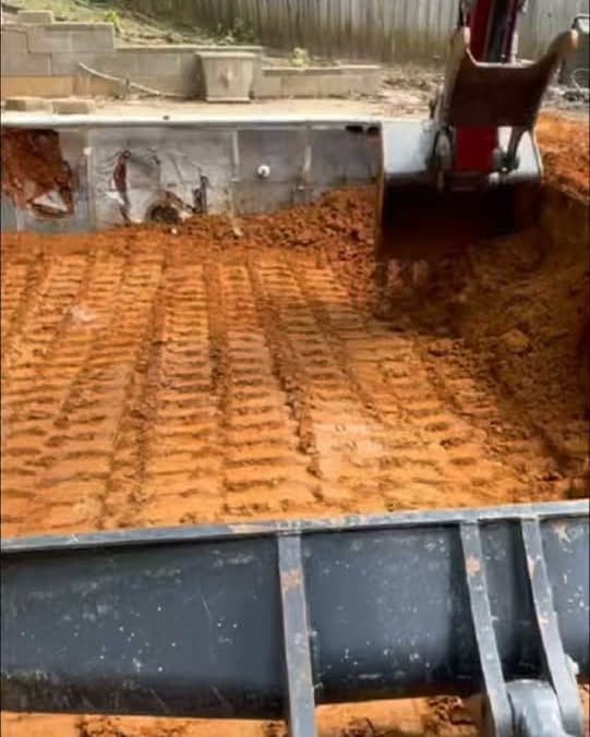 Excavator bucket over a freshly graded red dirt pad