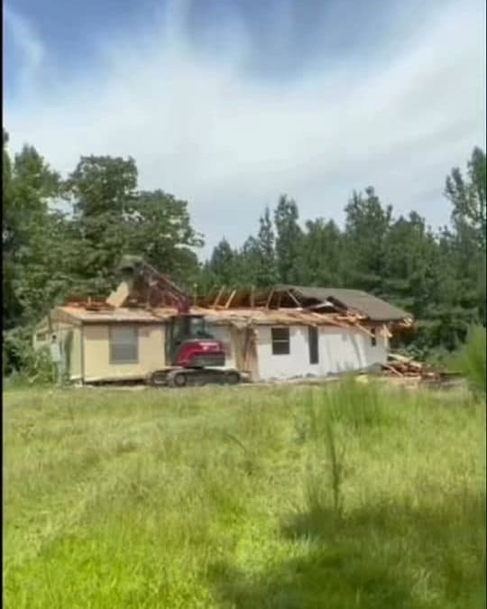 Excavator taking down an old house on a grassy lot